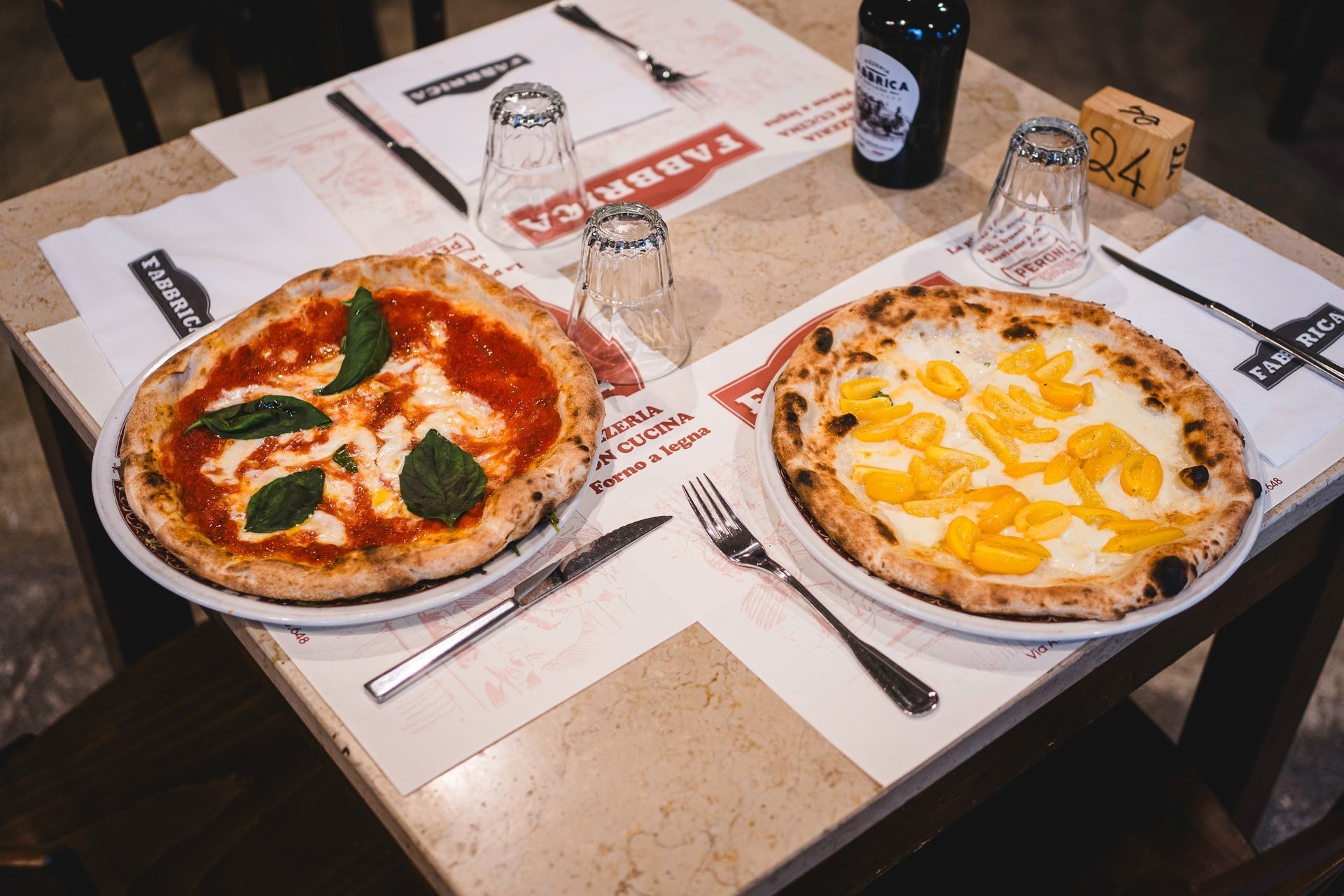 Due pizze fumanti sul tavolo con la tovaglietta rossa di Fabbrica